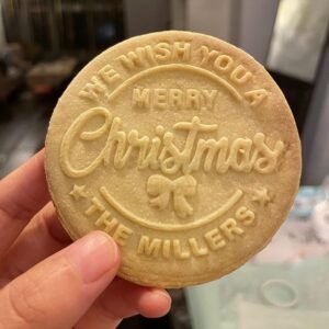 Hand holding a round Christmas cookie with "We Wish You a Merry Christmas" text